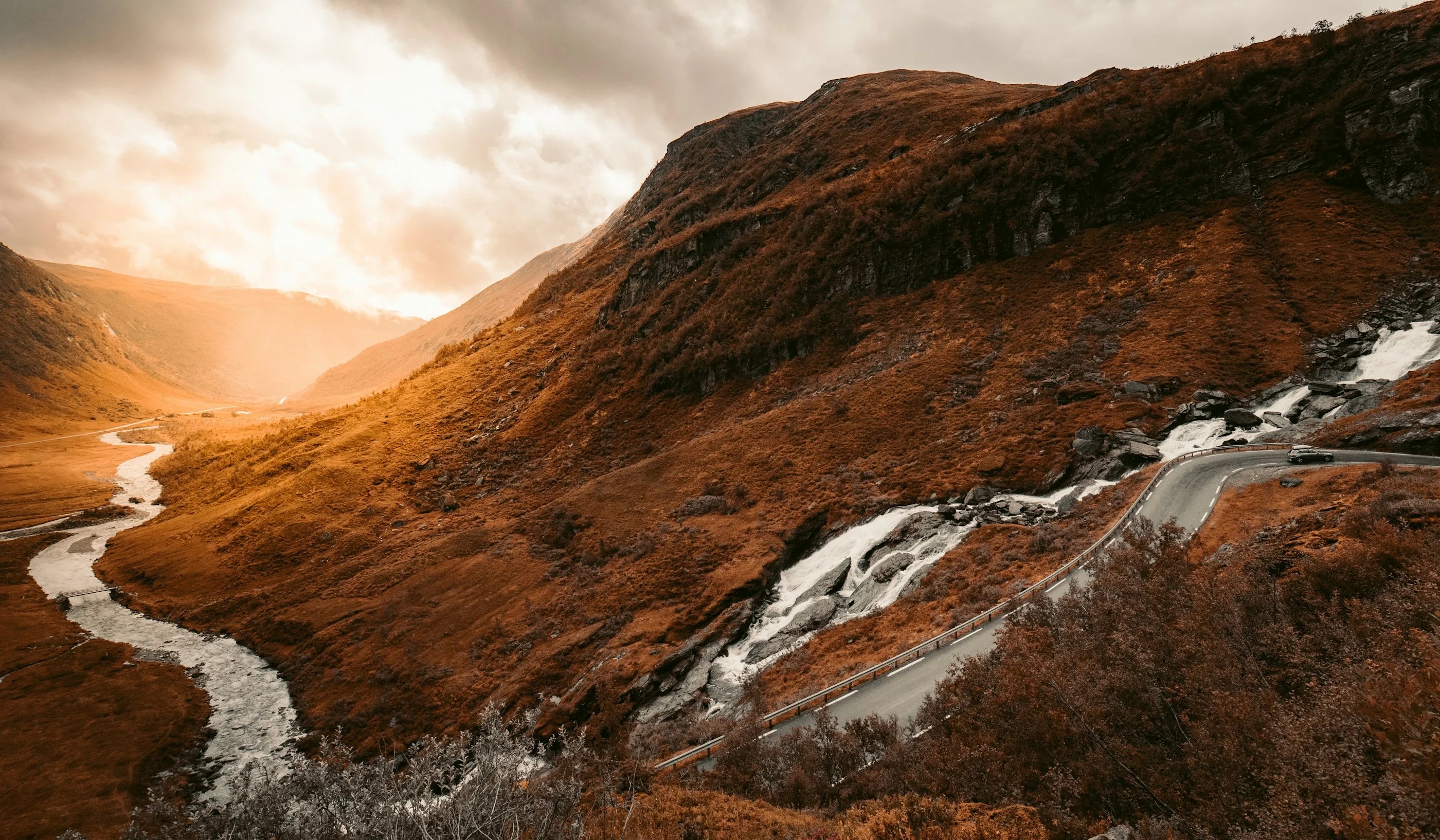 Winding road, waterfall and mountains in warm evening light in Myrkdalen, Norway.